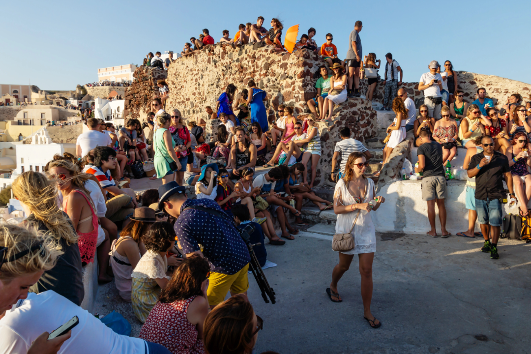 Touristen im Ort Oia auf Santorini bei Sonnenuntergang